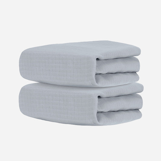 Two neatly folded light gray towels, stacked together against a white background, evoke the softness and comfort of Newton Baby's Breathable, Organic Cotton Sheets (2-pack).