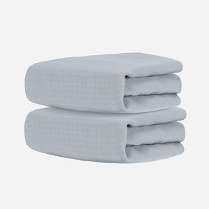 Two neatly folded light gray towels, stacked together against a white background, evoke the softness and comfort of Newton Baby's Breathable, Organic Cotton Sheets (2-pack).