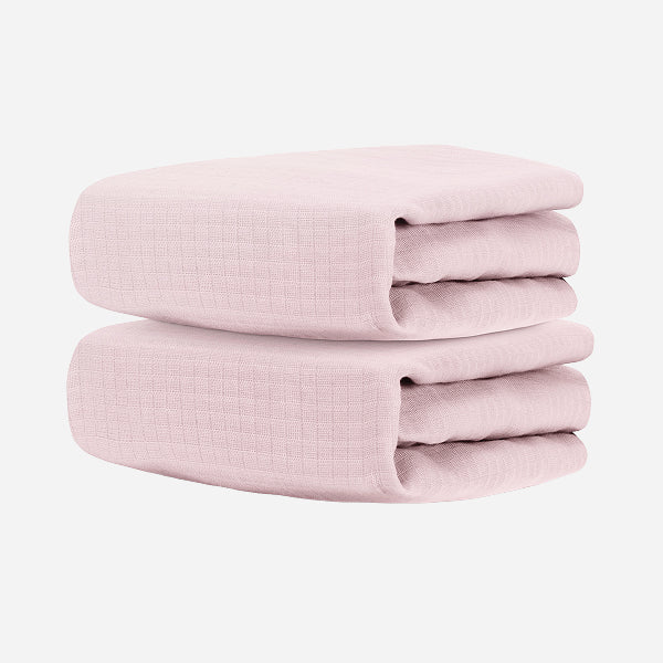 Two folded Newton Baby Breathable, Organic Cotton Sheets (2-pack), light pink in color, stacked against a plain white background.