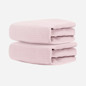 Two folded Newton Baby Breathable, Organic Cotton Sheets (2-pack), light pink in color, stacked against a plain white background.
