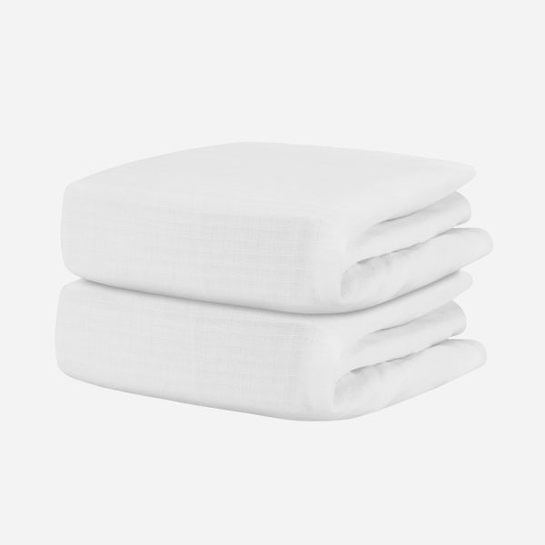 A stack of two neatly folded, white Newton Baby Breathable, Organic Cotton Sheets (2-pack) rests against a plain white background.