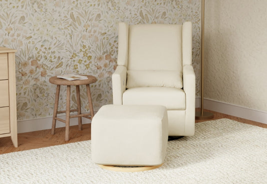 A cozy nursery corner featuring a cream-colored glider chair with a matching ottoman, set against a floral wallpaper backdrop, with a wooden side table and a white rug on the floor.