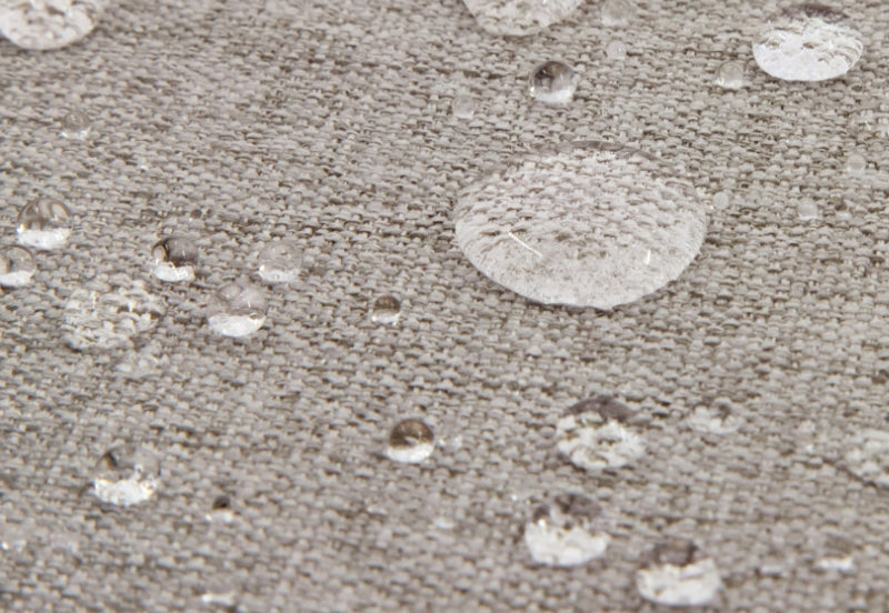 Close-up view of water droplets on a textured gray fabric surface, demonstrating waterproof material.