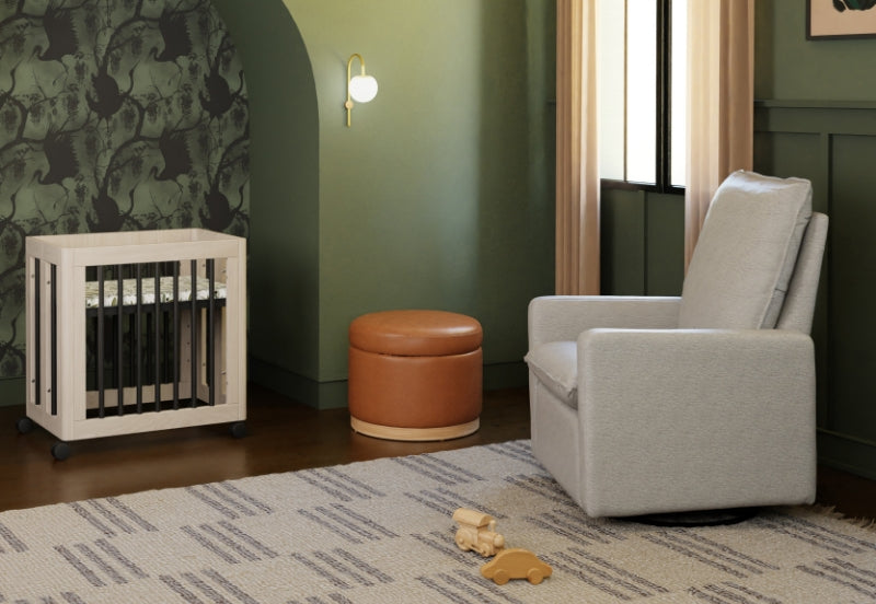 A cozy nursery featuring a grey chair, a white crib, and soft toys on a patterned rug, set against a green walled background with stylish decor.