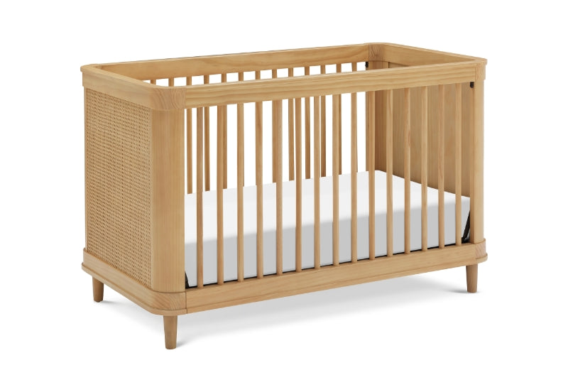 Modern wooden baby crib with a white mattress, featuring slatted sides and a rattan end panel.