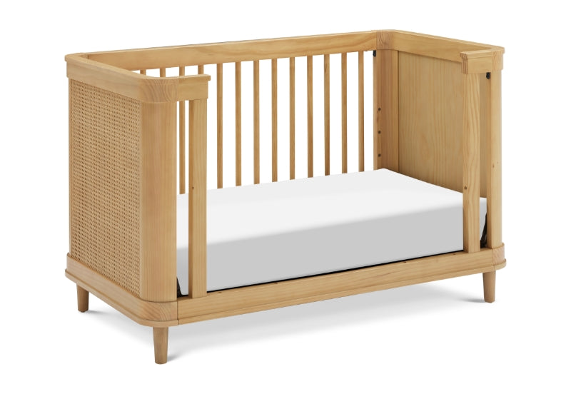 Wooden baby crib with a white mattress, featuring vertical bars and rattan side panels, isolated on a white background.