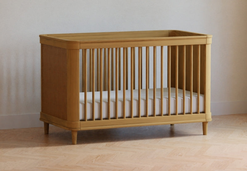 Traditional wooden crib in a light tan color positioned on a hardwood floor against a neutral wall background.