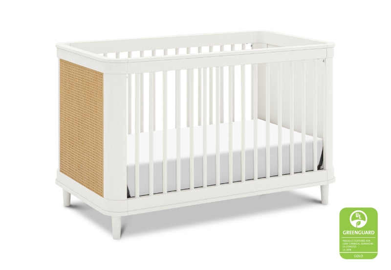 White crib with a beige rattan detail and a Greenguard Gold certification logo on the right corner.