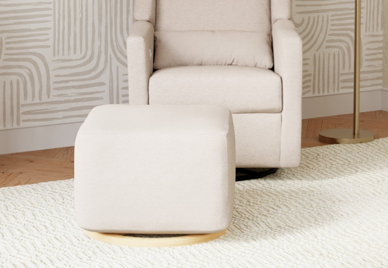 A modern beige nursery glider chair with a matching ottoman on a textured white rug, positioned in a soothing, neutral-toned room.