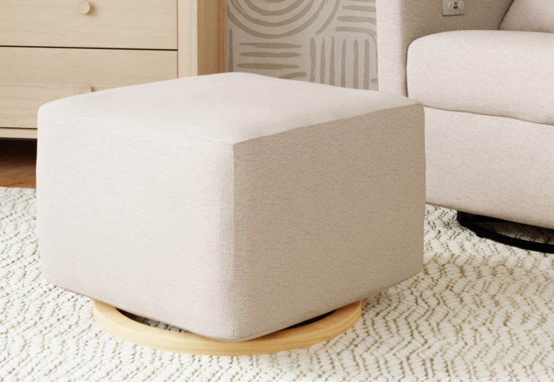 Modern beige nursery ottoman on a wooden base set beside a cabinet and an armchair in a cozy room setting.