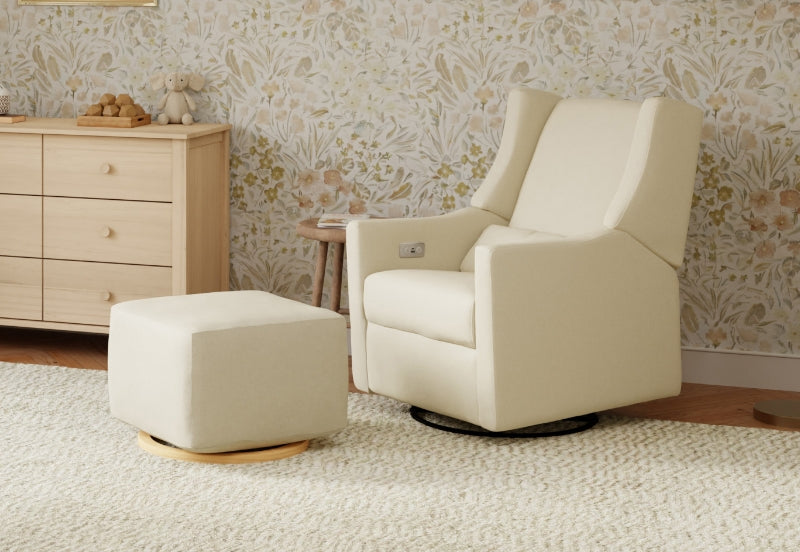 A cozy nursery room featuring a beige glider chair and matching ottoman, beside a light wooden dresser against a floral wallpaper backdrop.