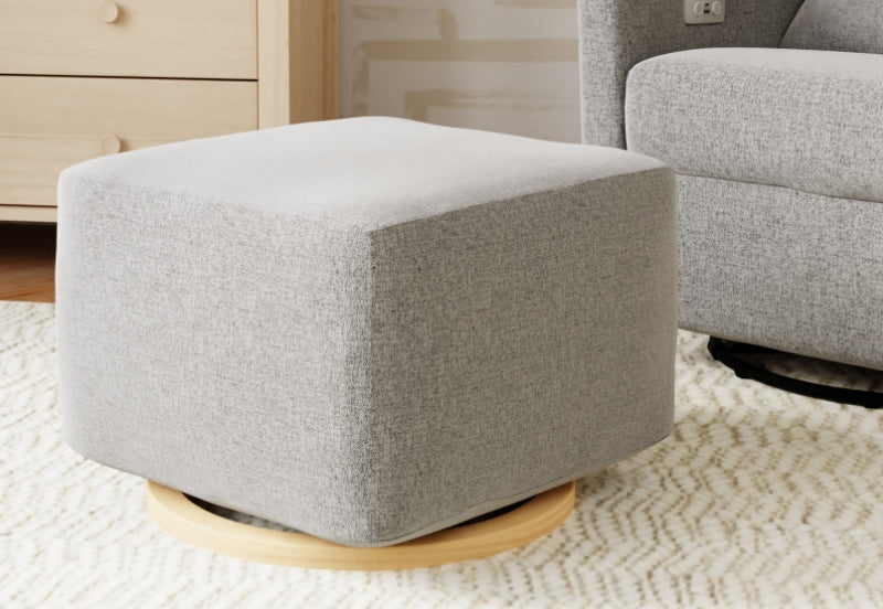 Modern gray and white nursery ottoman on a wooden base, set against a subtly detailed rug and a glimpse of furniture.