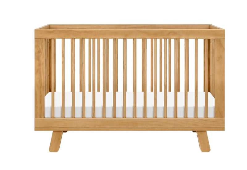 A modern wooden baby crib with a white mattress, isolated on a white background.