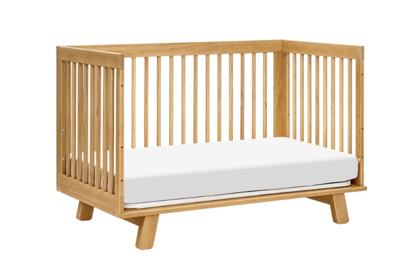 Modern wooden baby crib with a white mattress on a plain background.