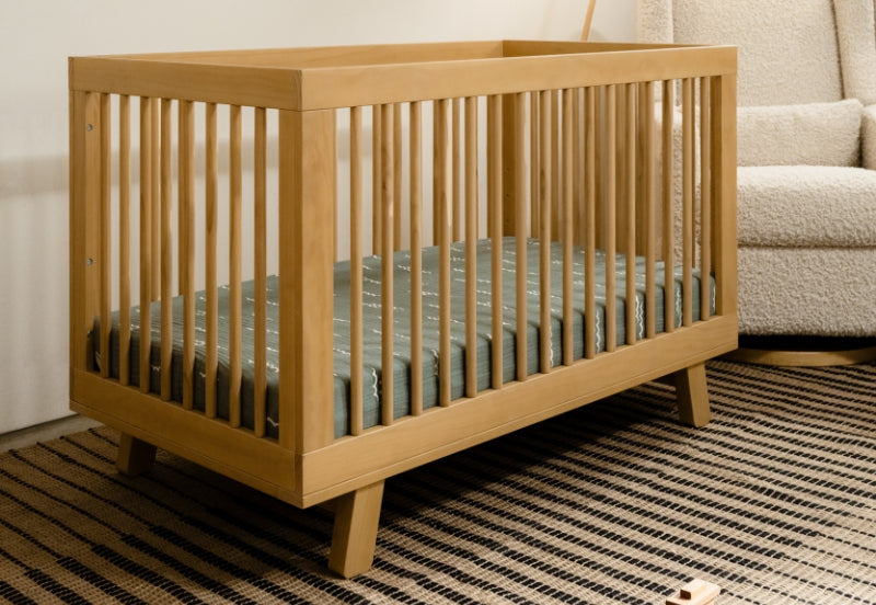 Wooden baby crib in a cozy room, set on a striped rug with a plush chair and wooden toys nearby.