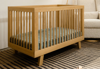 Wooden baby crib in a cozy room, set on a striped rug with a plush chair and wooden toys nearby.
