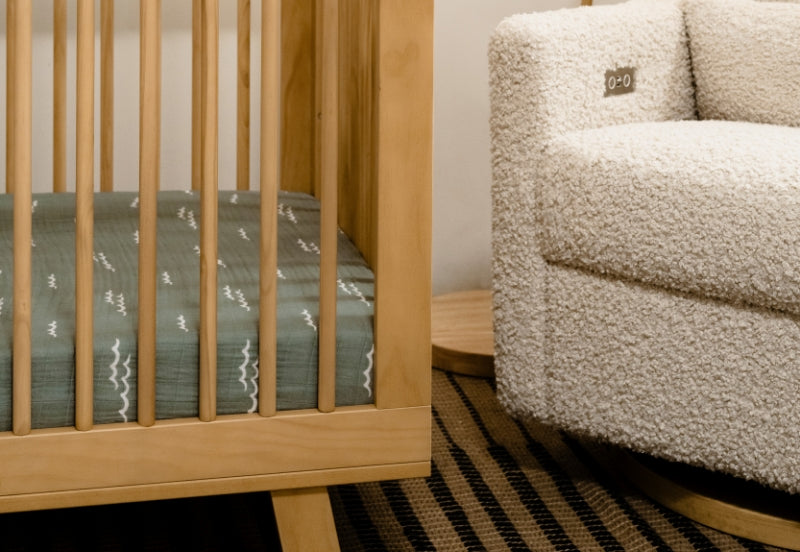 Wooden crib with a breathable mattress beside a plush, armless chair in a cozy nursery setting.