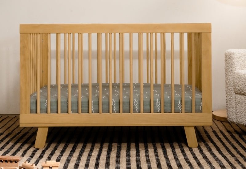 A minimalist wooden crib with a patterned mattress displayed in a cozy, neutral-toned nursery.