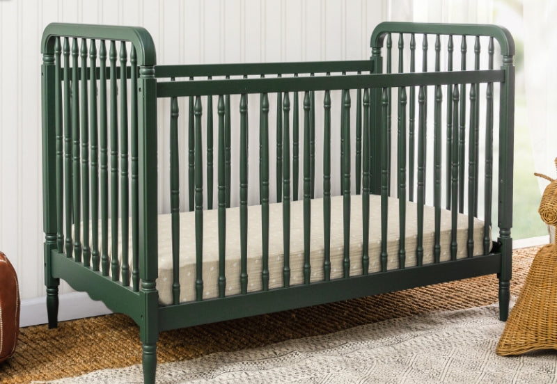 Elegant dark green crib with a classic spindle design, displayed in a cozy room with a wicker basket and a woven rug.