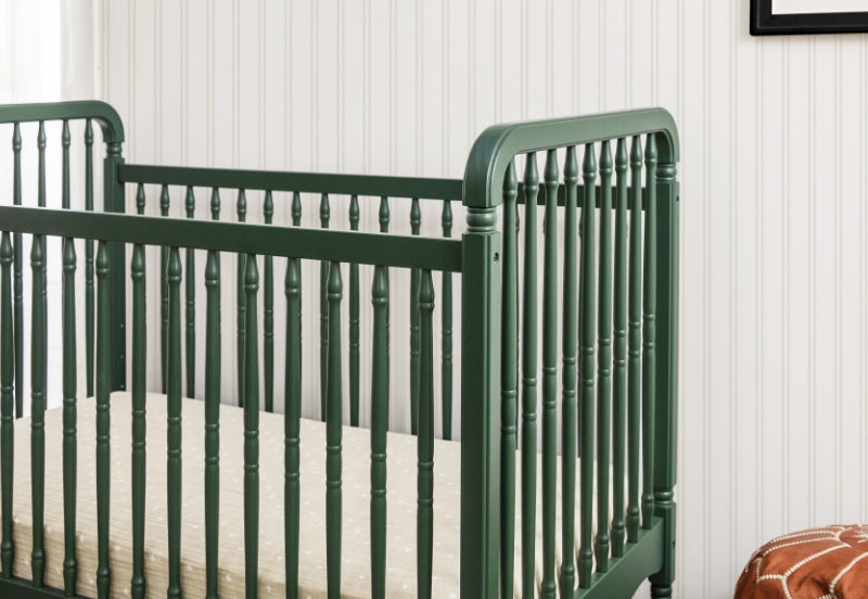 Dark green traditional crib against a white vertical striped wallpaper background.