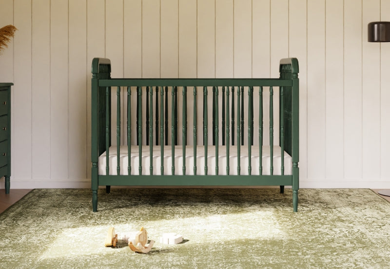 Green baby crib in a sunlit nursery with white paneling on the wall and a few toys on a rug.