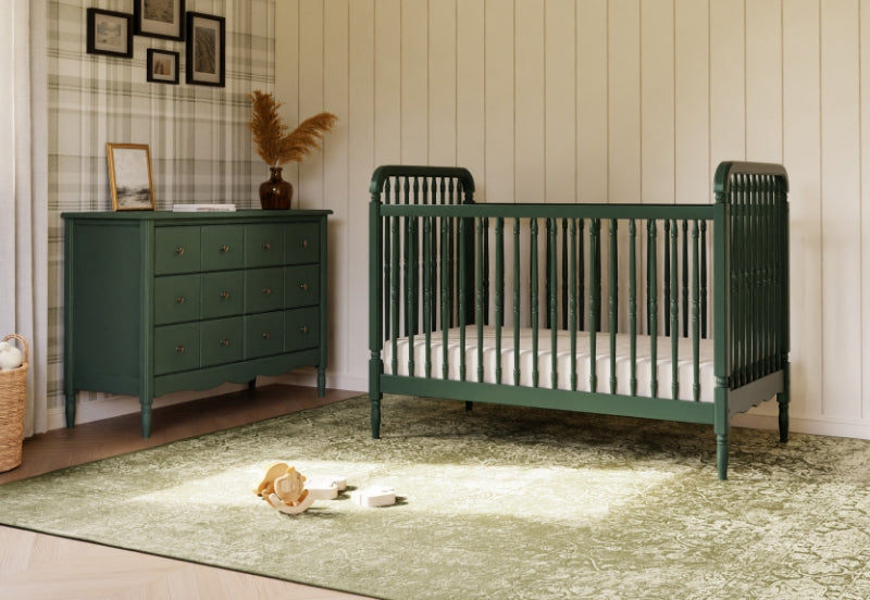 A stylish nursery featuring a dark green crib next to a matching dresser on a textured green rug, with subtle decor and natural light filling the room.