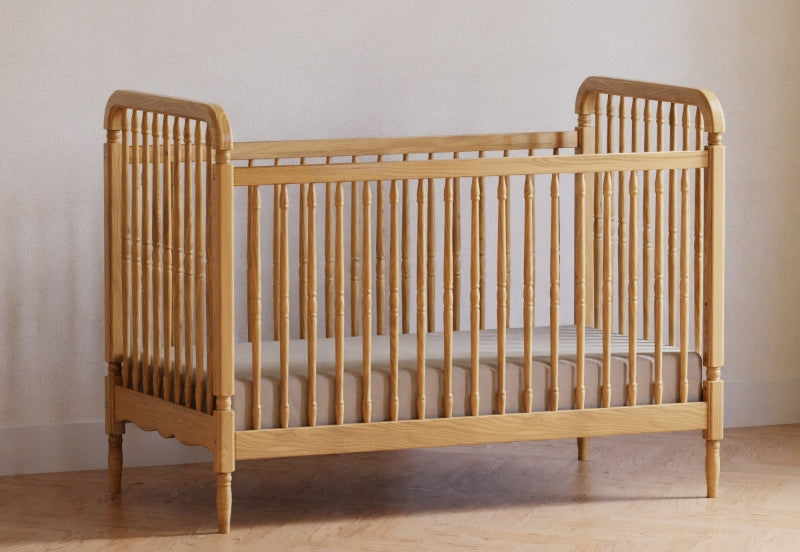 Classic wooden baby crib in a warm natural finish against a simple, neutral wall, positioned on a hardwood floor.
