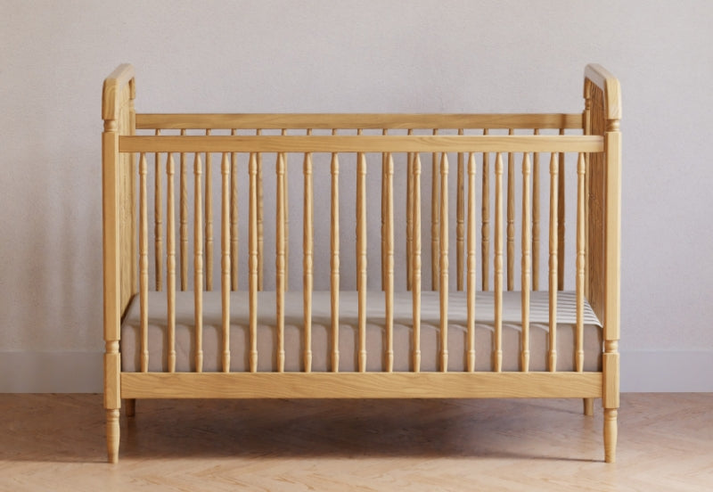 Classic wooden crib in a neutral room with a striped mattress.