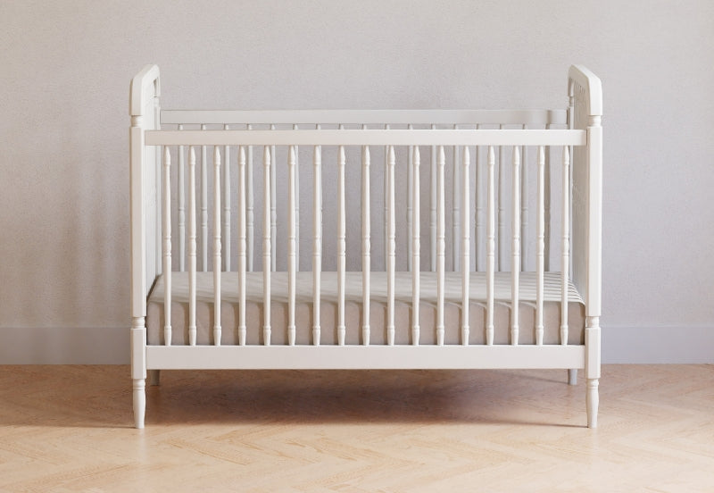 A simple white crib positioned against a neutral wall on a hardwood floor. 