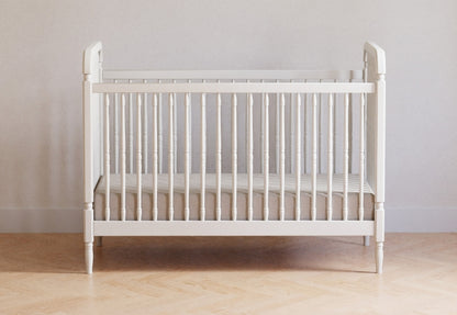 A simple white crib positioned against a neutral wall on a hardwood floor. 