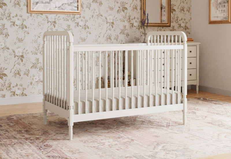 White baby crib in a vintage-styled nursery room with floral wallpaper and a patterned rug.
