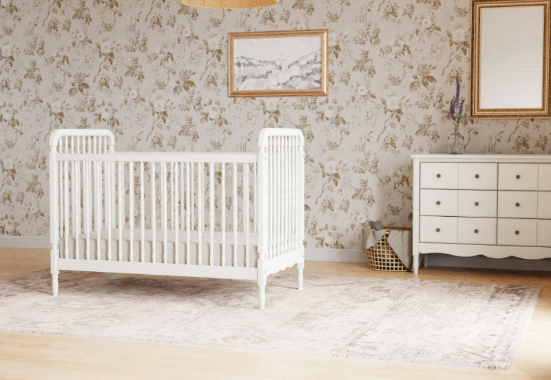 Elegant nursery room featuring a white crib, a matching dresser, and floral wallpaper with framed artwork.