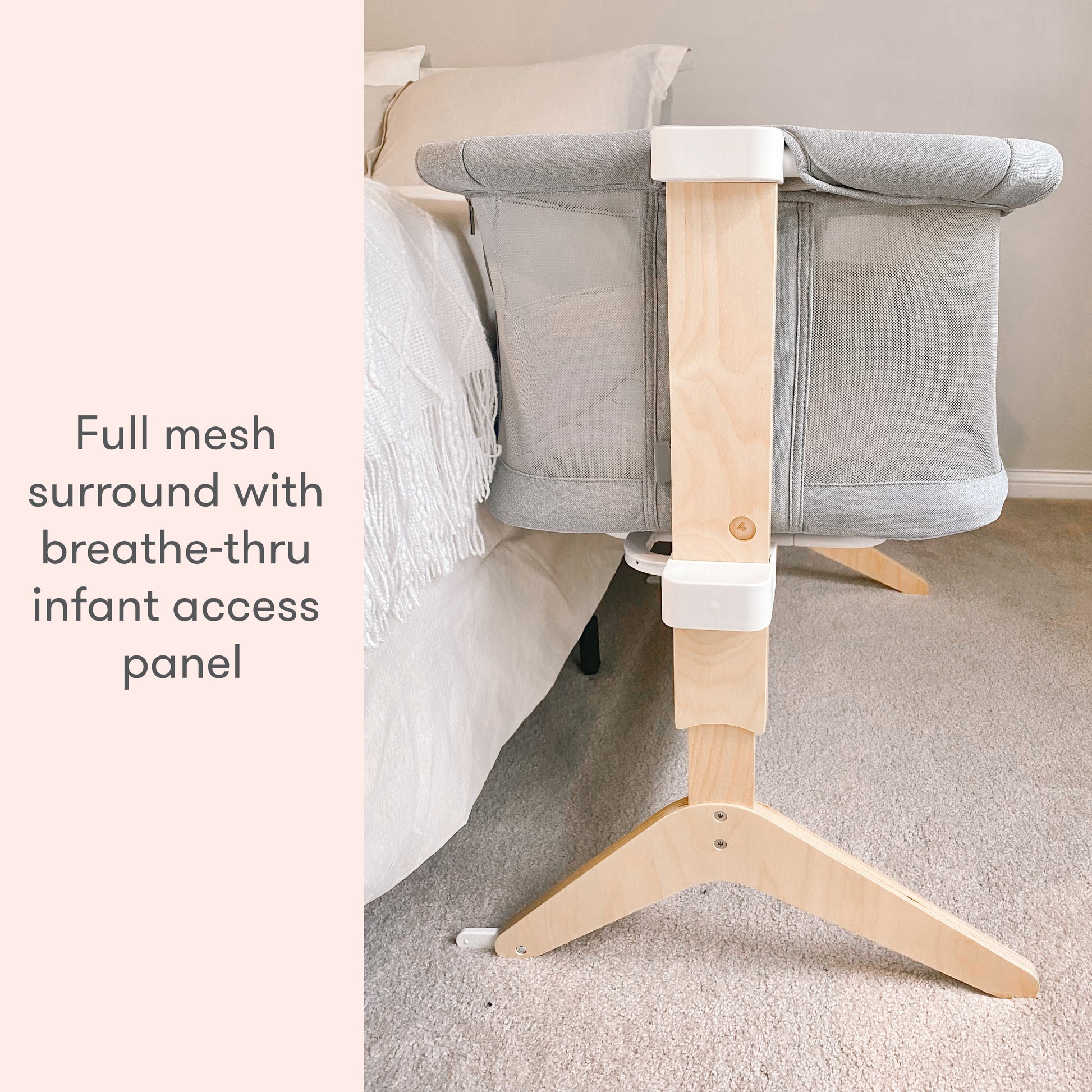 A modern gray baby bassinet with wooden legs placed in a serene room, featuring the text 'full mesh surround with breathe-thru infant access panel."