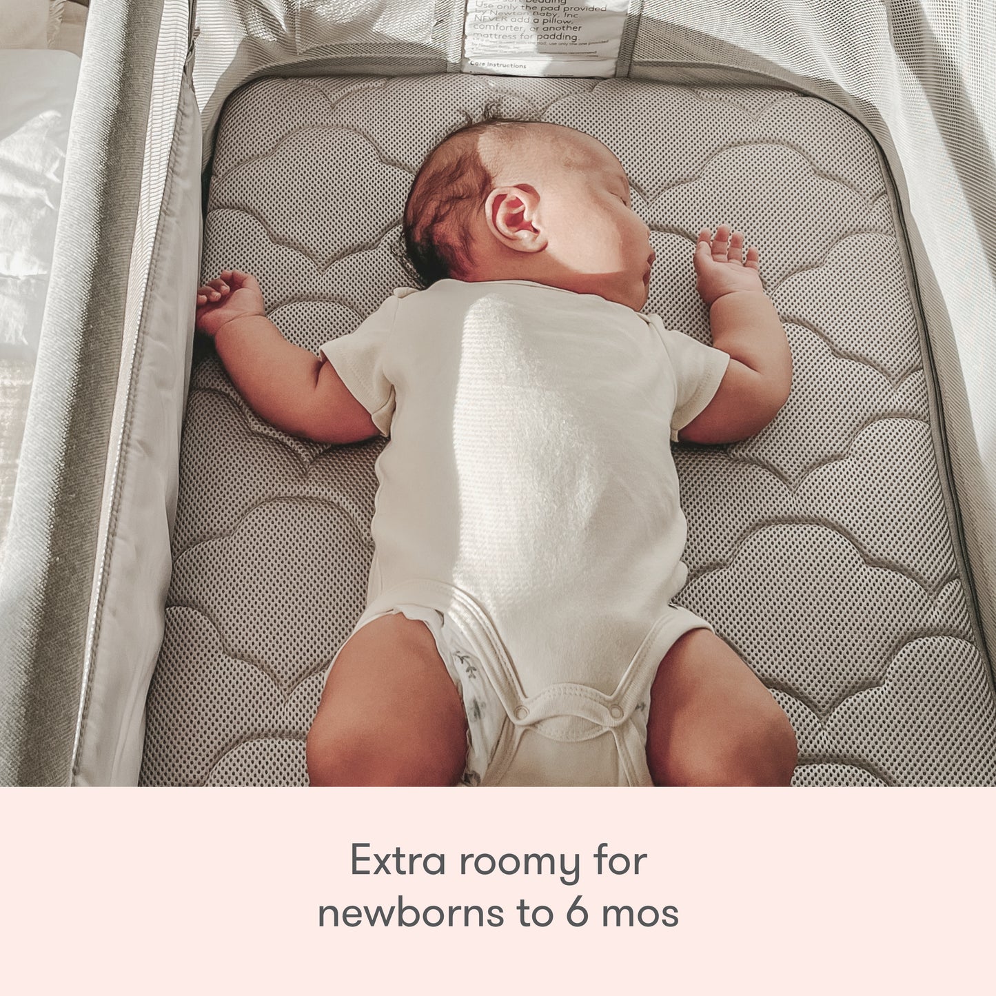 A baby sleeps on its back in the spacious Newton Baby Bassinet & Bedside Sleeper with a cloud-patterned Wovenaire mattress. Text below reads: “Extra roomy for newborns to 6 mos.”.