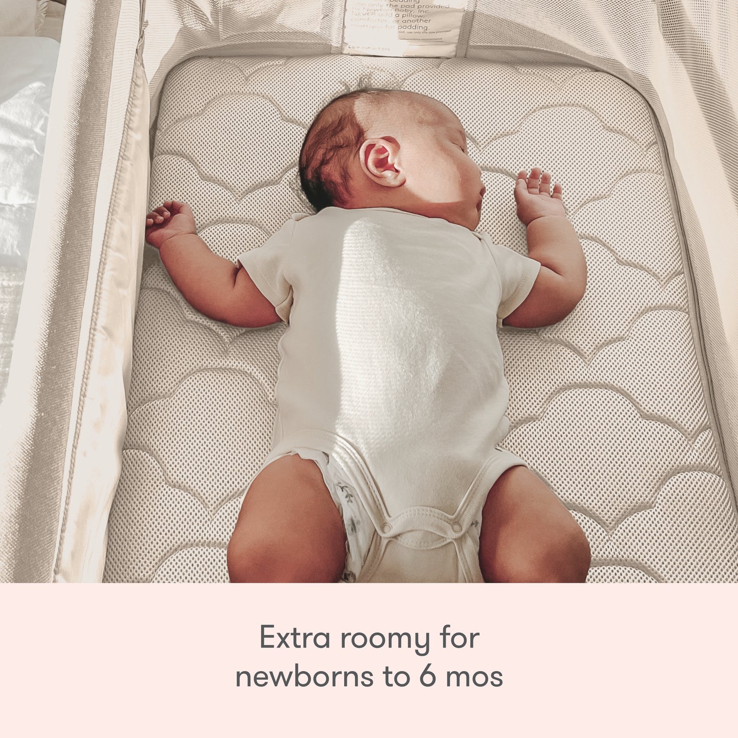 A baby in a white onesie sleeps on their back in the Newton Baby Bassinet & Bedside Sleeper. Text below: Extra roomy for newborns to 6 months.