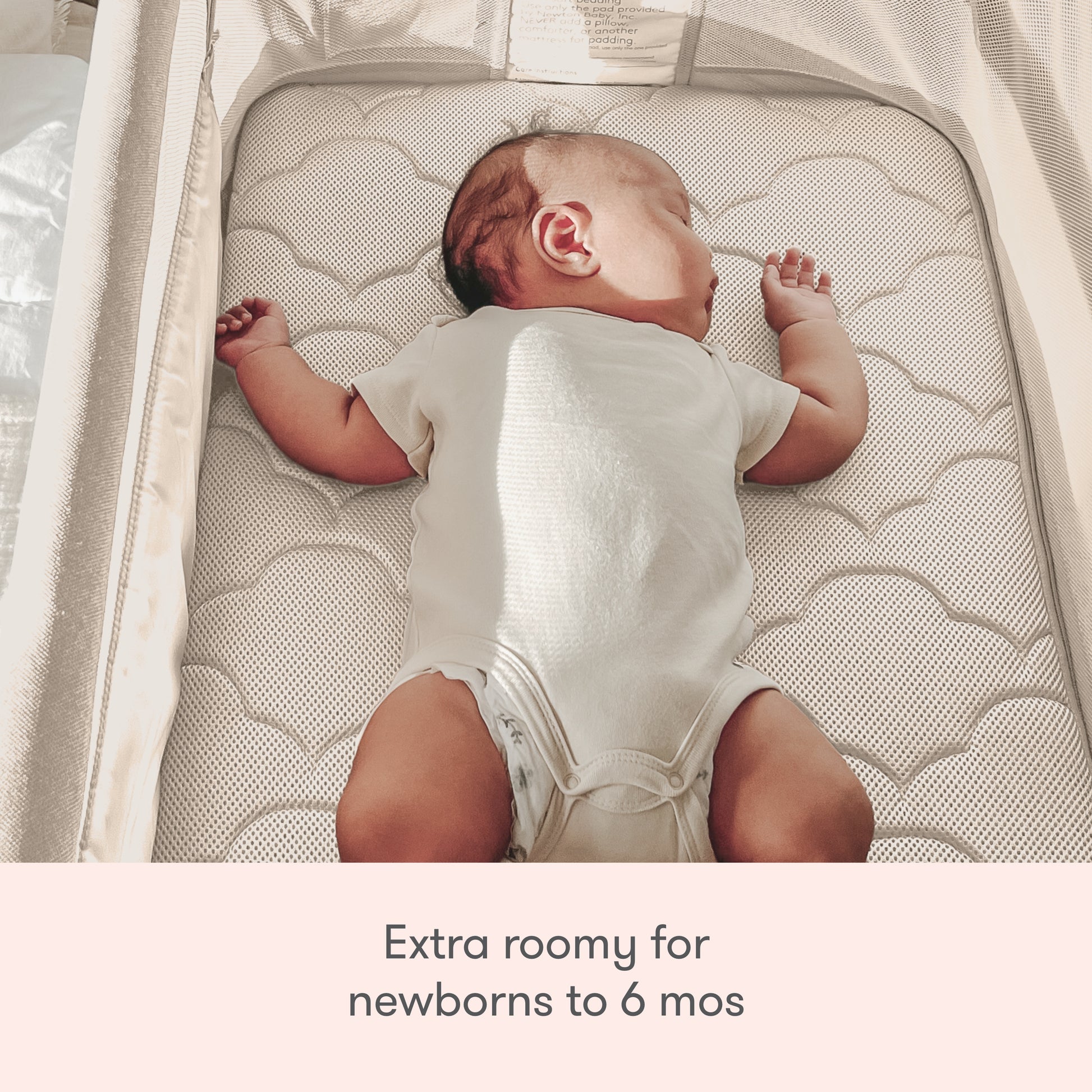 A baby in a white onesie sleeps on their back in the Newton Baby Bassinet & Bedside Sleeper. Text below: Extra roomy for newborns to 6 months.
