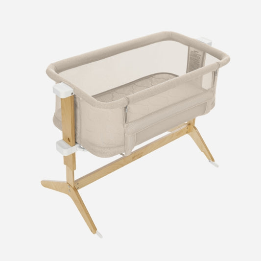 The Newton Baby Bassinet & Bedside Sleeper in beige features mesh sides, a breathe-thru mattress, and a wooden frame with angled legs and white plastic connectors, displayed against a plain white background. skip