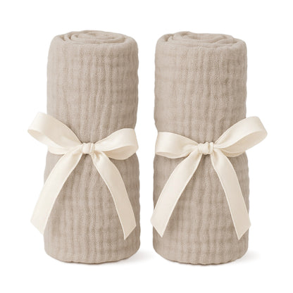 Two beige, textured blankets tied with cream ribbon bows stand upright side by side—an ideal pairing with Newton Baby Bassinet Extra Sheets for your bassinet or bedside sleeper. 999-8401-SAN