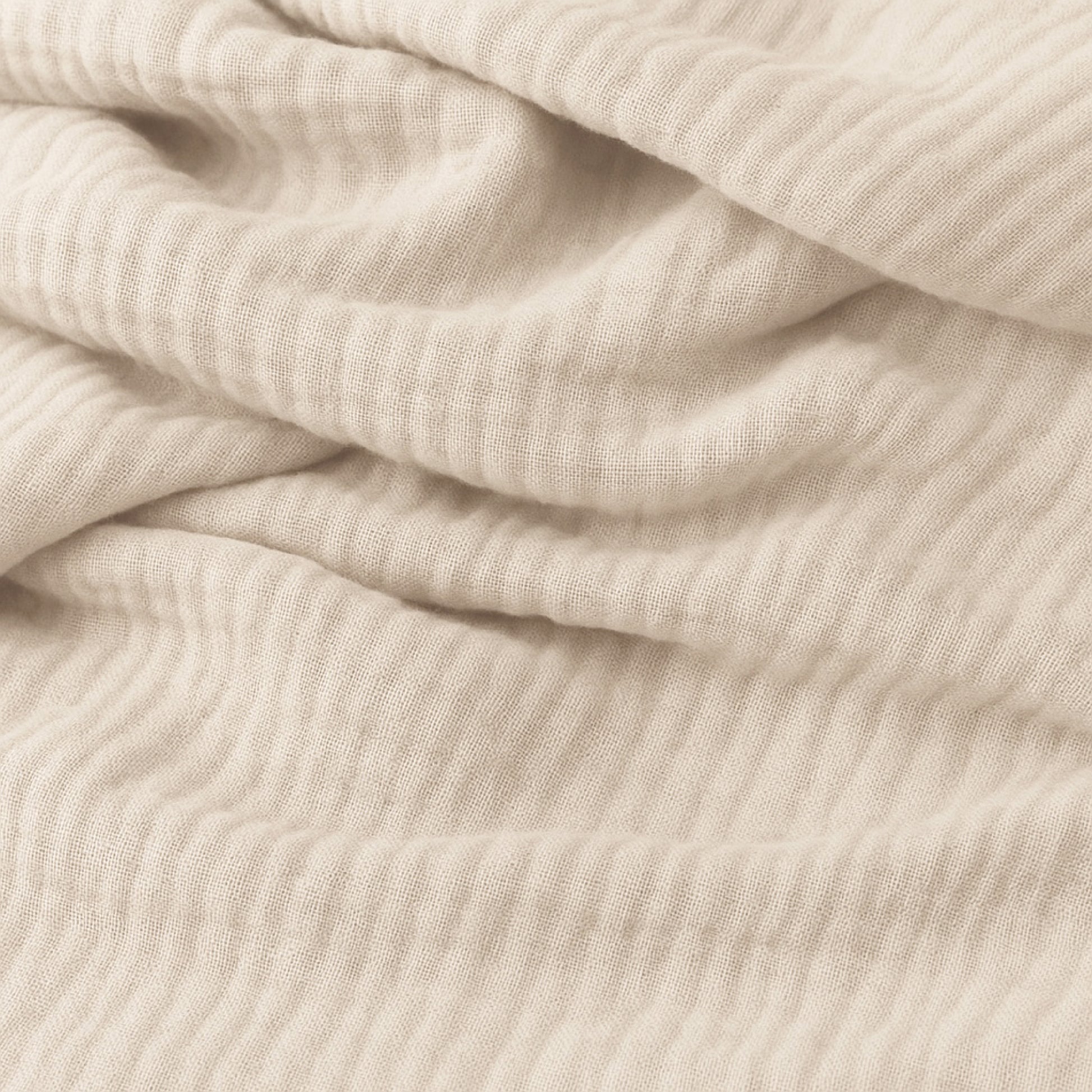 Close-up of soft, light beige ribbed fabric with gentle folds, resembling cozy cotton muslin, creates an inviting look—perfect for Newton Baby Bassinet Extra Sheets for your bedside sleeper.