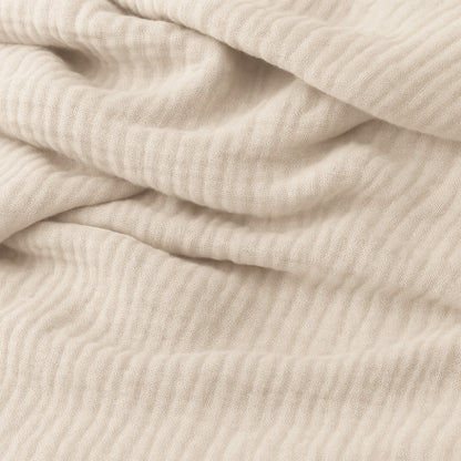 Close-up of soft, light beige ribbed fabric with gentle folds, resembling cozy cotton muslin, creates an inviting look—perfect for Newton Baby Bassinet Extra Sheets for your bedside sleeper.