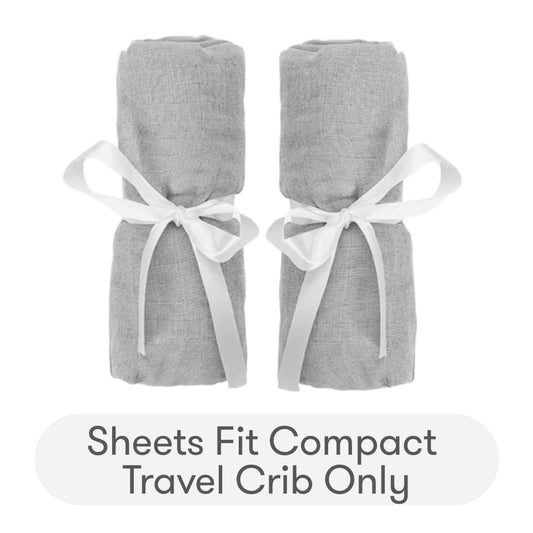 Two rolled-up gray Newton Baby Compact Travel Crib Sheets, each tied with a white ribbon, are shown side by side above text stating: Sheets fit Compact Travel Crib only—ideal for use as travel crib sheets or play yard mattress sheets.
