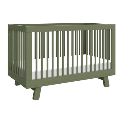 The Babyletto Hudson Convertible Crib features a modern olive green design with slatted sides, angled legs, and a white mattress—ideal for transitioning from crib to toddler bed as your child grows.