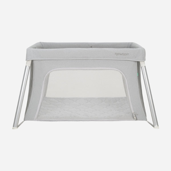 The Newton Baby Compact Travel Crib & Play Yard features mesh sides, a zippered front opening, angled white legs, a breathable mattress, and washable fabrics. Shown in gray against a plain white background.