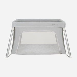 The Newton Baby Compact Travel Crib & Play Yard features mesh sides, a zippered front opening, angled white legs, a breathable mattress, and washable fabrics. Shown in gray against a plain white background.