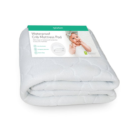 A folded, white Waterproof Crib Mattress Pad by Newton Baby features a green and white label with a baby in a bow headband. The label highlights its breathable, waterproof design—ideal for potty training.