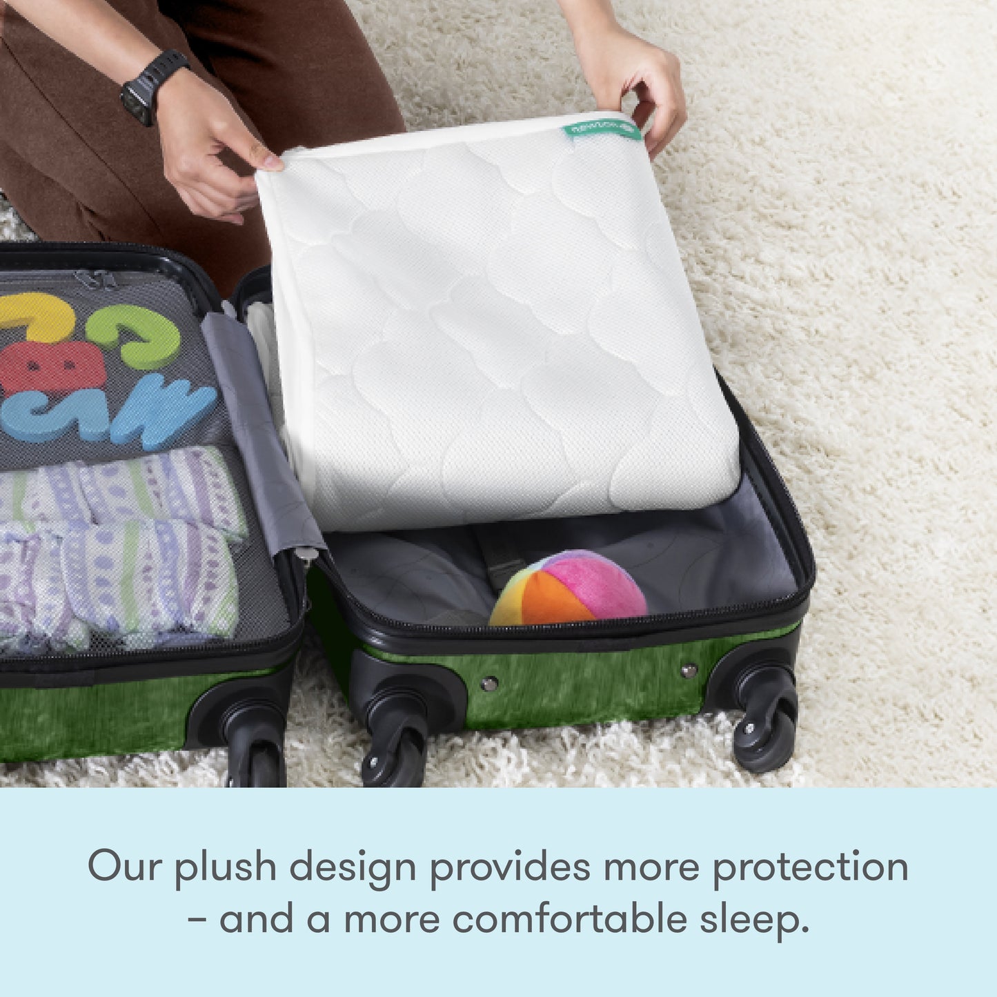 A person packs a Newton Baby Waterproof Crib Mattress Pad into a green suitcase, next to folded clothes and a colorful ball. Text below reads: Our plush design offers extra protection and ensures your baby sleeps more comfortably.