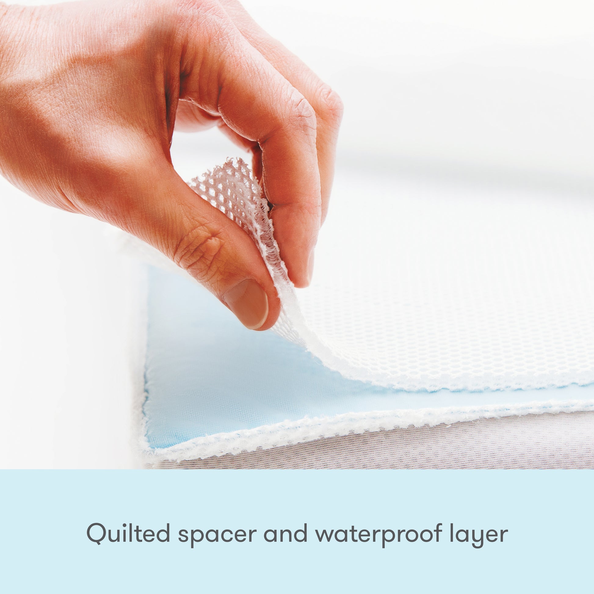 A hand lifts the quilted layer of a Newton Baby Waterproof Crib Mattress Pad, revealing the blue waterproof backing. Text: Quilted spacer and waterproof layer—ideal for potty training.