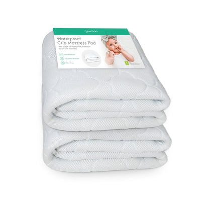 The Newton Baby Waterproof Crib Mattress Pad, shown folded in packaging with a baby and product info, offers waterproof protection, breathability, and easy machine washing—perfect for potty training or use as an ultra-breathable mattress pad.