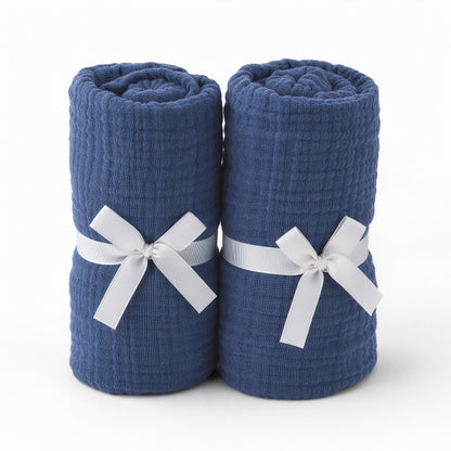 Two dark blue rolled towels, upright and tied with white ribbon bows, evoke the softness of Newton Baby's Breathable, Organic Cotton Sheets (2-pack), set against a plain white background.