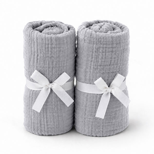 Two rolled-up light gray towels tied with white ribbons rest side by side, evoking the softness and purity of Newton Baby's Breathable, Organic Cotton Sheets (2-pack), set against a plain white background.